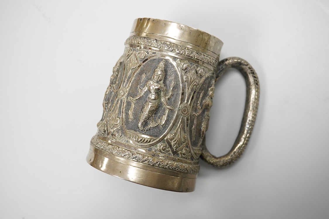 A 19th Century Indian white metal mug, embossed with deities, 11.1cm.